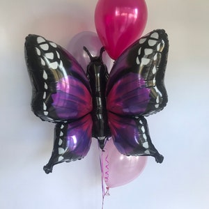 Pu&ograve; includere: Un gruppo di palloncini, tra cui un grande palloncino a forma di farfalla con ali nere e viola. I palloncini di accompagnamento sono rosa e magenta. Il palloncino a farfalla ha dettagli bianchi e un corpo nero.