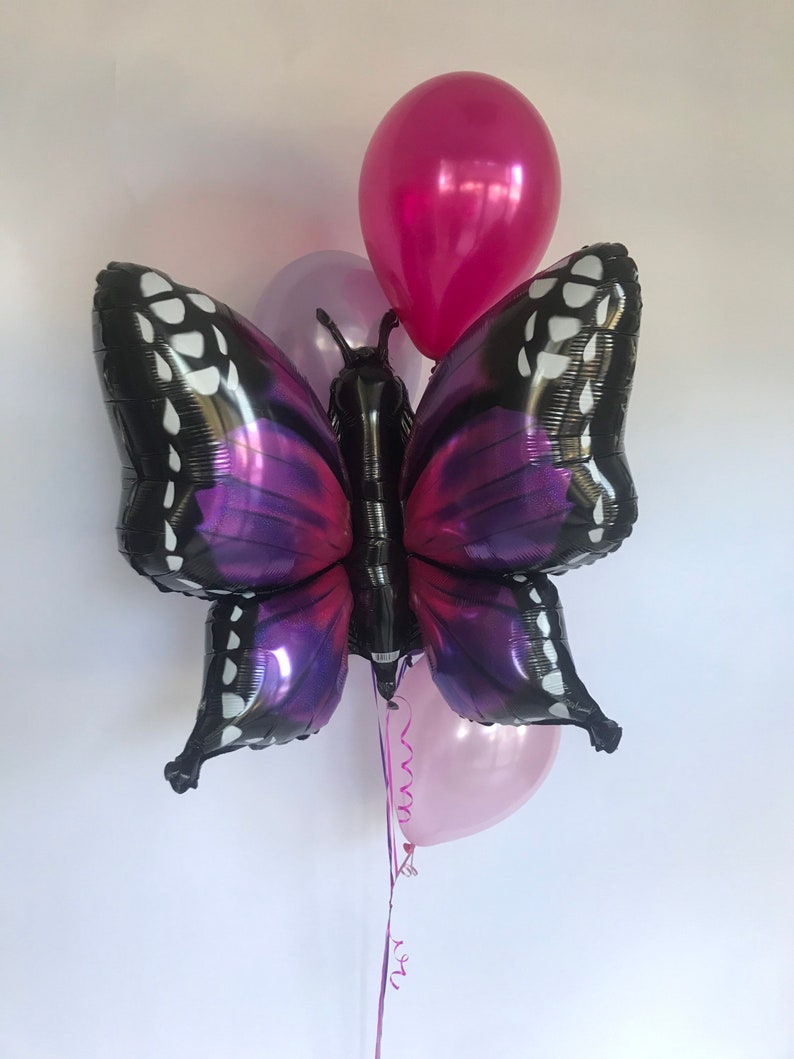 Pu&ograve; includere: Un gruppo di palloncini, tra cui un grande palloncino a forma di farfalla con ali nere e viola. I palloncini di accompagnamento sono rosa e magenta. Il palloncino a farfalla ha dettagli bianchi e un corpo nero.
