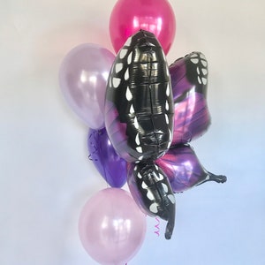 Pu&ograve; includere: Un gruppo di palloncini nei toni del rosa, viola e nero. Il pezzo forte &egrave; un palloncino a forma di farfalla con ali nere e pois bianchi. Altri palloncini sono rotondi e in tinta unita, creando una composizione festosa.
