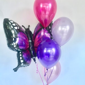 Pu&ograve; includere: Un grappolo di palloncini nei toni del viola, rosa e magenta. Il pezzo forte &egrave; un grande palloncino a forma di farfalla con ali nere e viola. Altri palloncini rotondi sono legati con nastri, creando una composizione festosa.