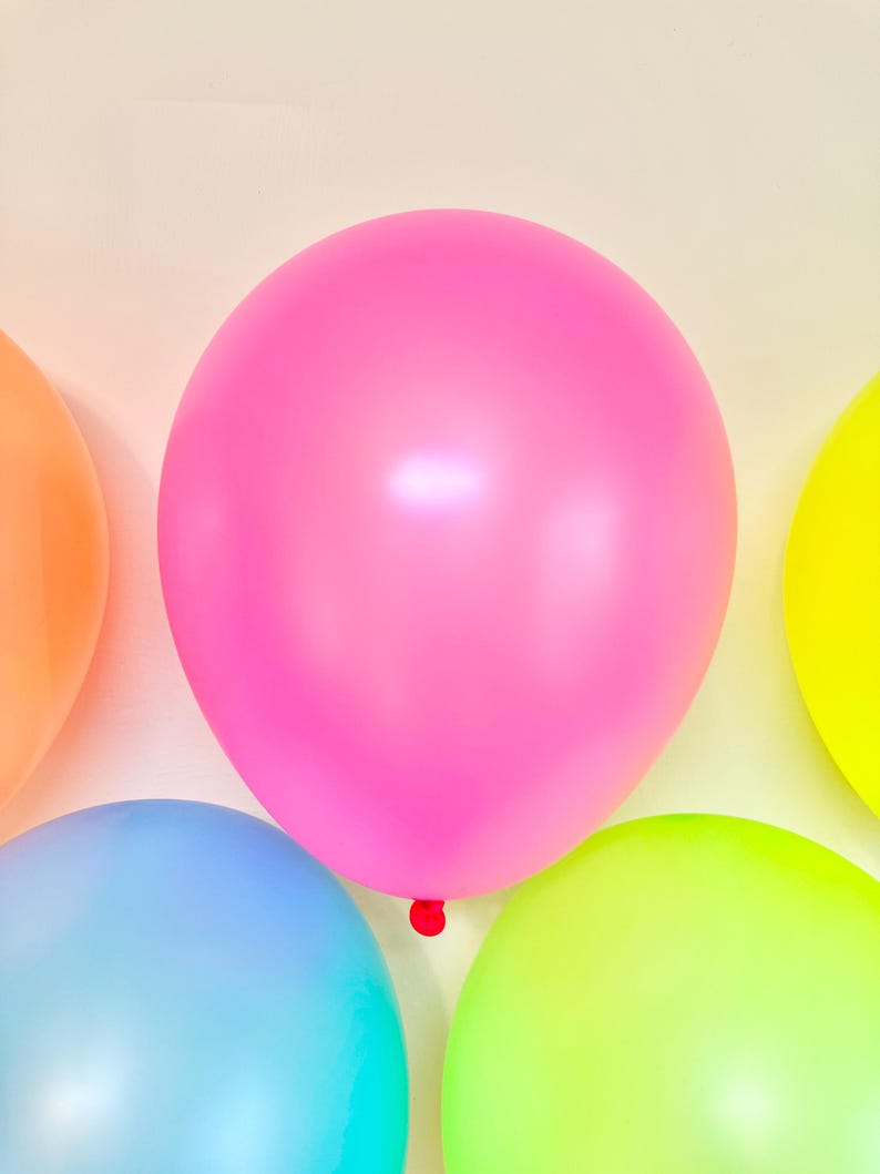 May include: Five colourful balloons in various shades of pink, blue, green, and yellow. The balloons are arranged in a semi-circle on a white background.