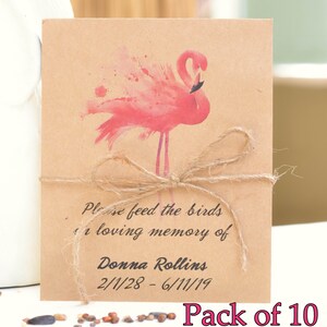 Op de afbeelding: Een bruin papieren pakketje met een roze flamingo-illustratie en touw eromheen gebonden. Het pakketje heeft de tekst "Please feed the birds in loving memory of Donna Rollins 2/1/28 - 6/11/19". De tekst "Pack of 10" is zichtbaar onder het pakketje.