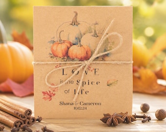 May include: A square tan card tied with twine featuring a watercolor illustration of pumpkins and autumn leaves. The text reads: Love is the spice of life, Shana & Cameron, 10.12.24. The card is decorated with small red leaf accents.