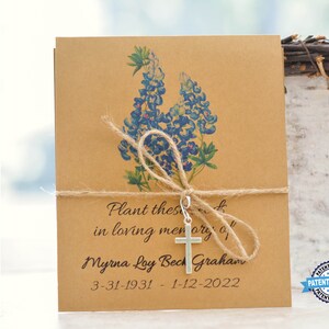 May include: Brown paper seed packet with a bluebonnet flower design and a silver cross charm. The packet has the text "Plant these seeds in loving memory of Myrna Loy Beck Graham 3-31-1931 - 1-12-2022".