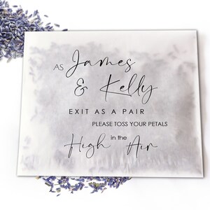 Op de afbeelding: Een wit papieren zakje met de tekst "AS James & Kelly EXIT AS A PAIR PLEASE TOSS YOUR PETALS in the High Air" in zwart script. Gedroogde lavendelbloemknoppen zijn rond het zakje verspreid.