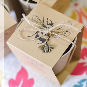 May include: A small brown paper box with a bee design and a gold bee charm. The box is tied with twine and has the text "Wildflower Garden Seed Kit" printed on the side.