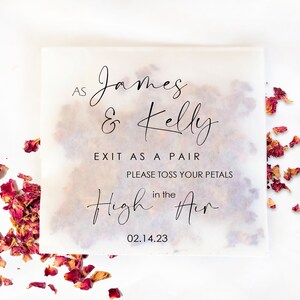 Op de afbeelding: Een vierkant, doorschijnend papieren zakje gevuld met gedroogde rozenblaadjes, met de tekst "As James & Kelly EXIT AS A PAIR PLEASE TOSS YOUR PETALS in the High Air 02.14.23" in zwart script. Verspreide bloemblaadjes omringen het zakje.
