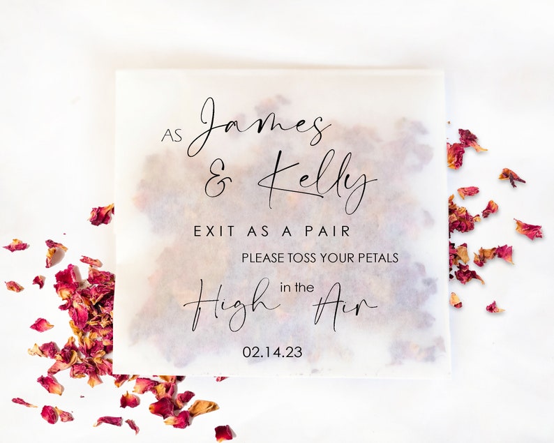 Op de afbeelding: Een vierkant, doorschijnend papieren zakje gevuld met gedroogde rozenblaadjes, met de tekst "As James & Kelly EXIT AS A PAIR PLEASE TOSS YOUR PETALS in the High Air 02.14.23" in zwart script. Verspreide bloemblaadjes omringen het zakje.