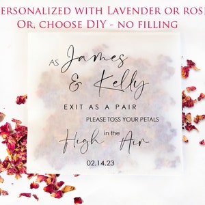 Op de afbeelding: Een vierkante, doorschijnende huwelijksbedankzak gevuld met gedroogde rozenblaadjes. De tas heeft een elegant script dat luidt "As James & Kelly Exit as a Pair, Please Toss Your Petals in the Air 02.14.23". De bovenste tekst luidt "GEPERSONALISEERD MET LAVENDEL OF ROOS OF, KIES DIY - GEEN VULLING".