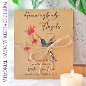 May include: A brown card with a hummingbird and flowers printed on it. The card has the text "Hummingbirds appear when Angels are near". The card is tied with twine and has a silver cross charm attached. The card also has the text "Scarce these wildflowers in loving memory of Vicki Ann Farn November 9, 1956-October 6, 2023".