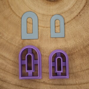 Puede incluir: Cuatro cortadores de galletas con forma de ventanas arqueadas. Dos son de color azul claro y dos son de color morado. Los cortadores morados tienen un rectángulo más pequeño cortado dentro del arco más grande.
