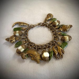 Puede incluir: Un brazalete de oro con dijes verdes y blancos. Los dijes tienen forma de peces, conchas marinas y otros objetos náuticos.