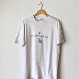 Puede incluir: Camiseta blanca con un gráfico de un ratón de ordenador con un logotipo de manzana arcoíris y el texto "Move over, Mickey."