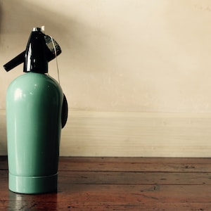 以下が含まれることがあります： 金属製のトップと白い紐が付いた、緑と黒のヴィンテージソーダサイフォンボトルです。