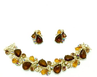 Op de afbeelding: Een gouden ketting en oorbellenset met bruine en amberkleurige, druppelvormige strasssteentjes. De ketting is in een rankontwerp met bladeren en bloemen.