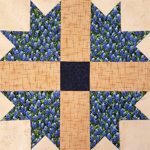 May include: A quilt block with a blue and green floral pattern in the center, surrounded by a tan and brown plaid pattern.