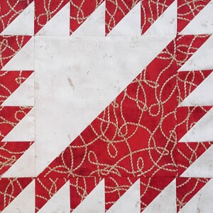 Puede incluir: Un bloque de colcha rojo y blanco con un patrón geométrico. La tela roja tiene un diseño de cuerda blanca.
