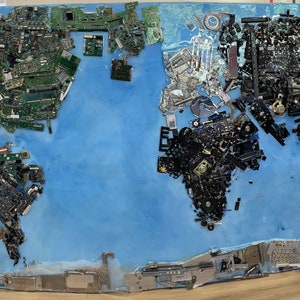 May include: A world map made of recycled computer parts, including circuit boards, wires, and other electronic components. The map is on a blue background and is framed in a wooden frame.