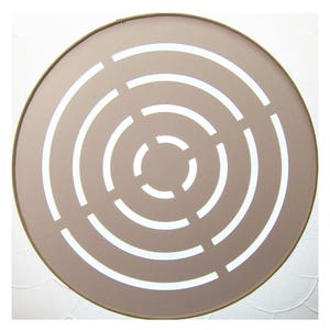 May include: A round, beige-coloured wall decor with a concentric circle design. The circles are white and create a geometric pattern.