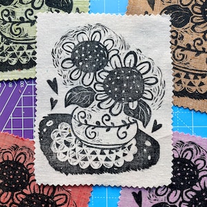 Peut inclure: Impression linogravure en noir et blanc de deux tournesols sur fond de lin blanc. Les tournesols sont dans un vase avec un motif décoratif. L'impression est encadrée d'une bordure blanche.