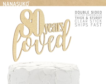 May include: Gold glitter cake topper with the text "80 years loved".