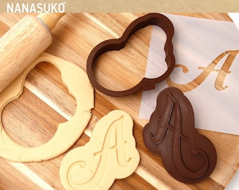 May include: A set of brown plastic cookie cutters in the shape of the letter "A" on a wooden cutting board. There is a rolling pin and a piece of dough in the background.