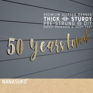 May include: Gold glitter banner with the text "50 years loved" on a gray wood background. The banner is pre-strung and comes with instructions for DIY assembly.  The banner is thick and sturdy, and is safely packaged and ships fast.
