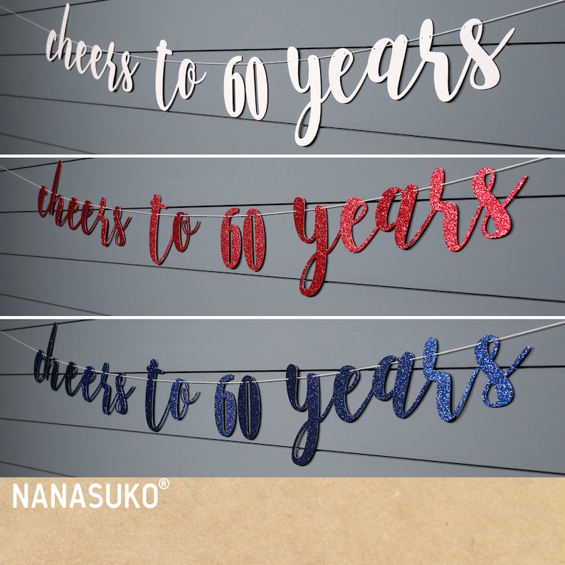 May include: Three banners with the text "cheers to 60 years" in a cursive font. The top banner is white, the middle is red glitter, and the bottom is blue glitter. The banners are strung on a thin white string.