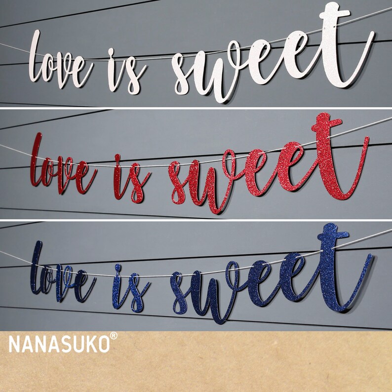 Puede incluir: Tres pancartas con el texto "love is sweet" en blanco, rojo con purpurina y azul con purpurina. Las pancartas est&aacute;n colgadas de una cuerda.