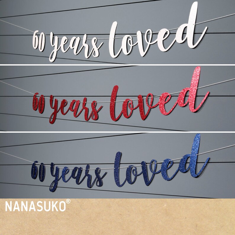 May include: Three banner decorations with the text "60 years loved" in white, red glitter, and blue glitter. The banners are strung on white twine.