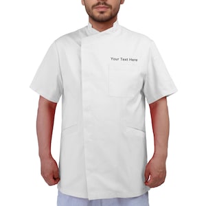 May include: A white chef's jacket with short sleeves, a mandarin collar, and a single chest pocket. The text "Your Text Here" is printed on the chest pocket. The jacket has a wrap-style closure and two lower pockets.
