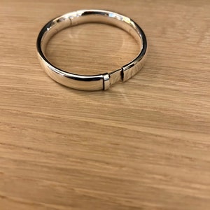 Könnte beinhalten: Ein silbernes Armreif-Armband mit einem Scharnierverschluss.