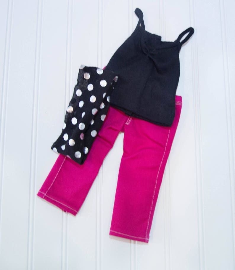 May include: A black tank top, pink pants, and a black and silver polka dot scarf. The outfit is for a doll.