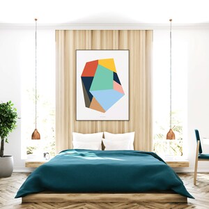 May include: A teal blue bedspread on a wooden bed frame with white pillows. A geometric abstract art print hangs on the wall above the bed. The room has a wooden floor, a potted plant, and a vanity with a round mirror.