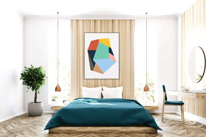 May include: A teal blue bedspread on a wooden bed frame with white pillows. A geometric abstract art print hangs on the wall above the bed. The room has a wooden floor, a potted plant, and a vanity with a round mirror.