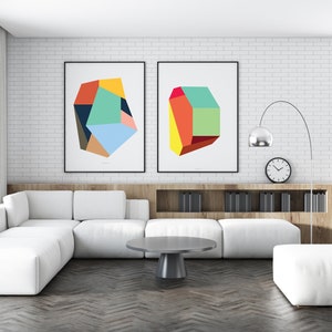 May include: Two abstract geometric art prints with colorful shapes in a modern living room with a white sectional sofa, a gray coffee table, and a white ottoman.