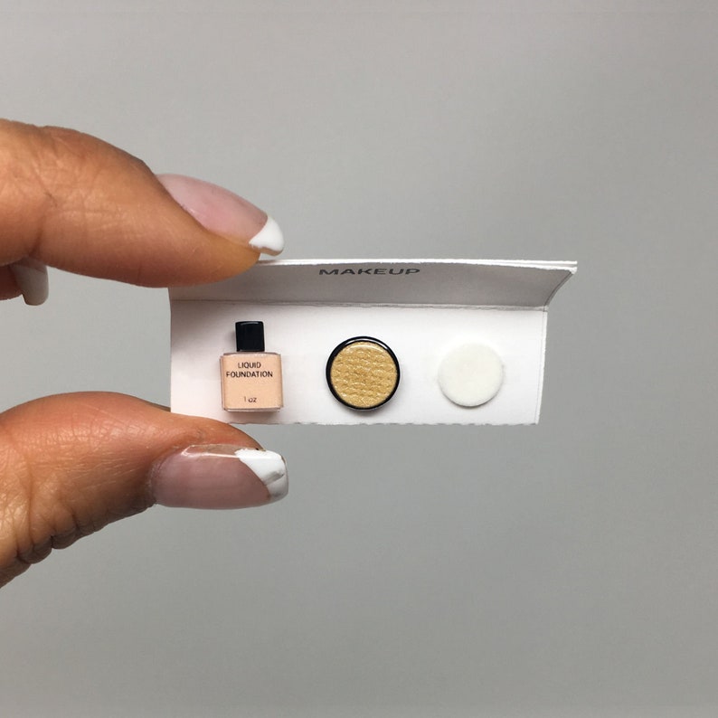May include: A miniature makeup set with a small bottle of liquid foundation labeled "Liquid Foundation 1 oz", a round gold-colored compact, and a white round compact. The set is labeled "MAKEUP" on the top.