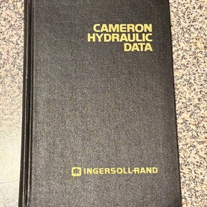 May include: A black hardcover book titled CAMERON HYDRAULIC DATA in gold lettering on the front cover. The bottom of the cover features the Ingersoll-Rand logo and name in gold text. The book has a textured finish and a vertical spine on the left.