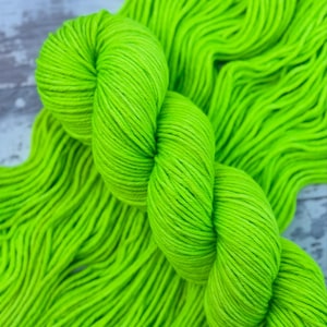 May include: Close-up of bright neon green yarn. The yarn is tightly wound into a skein, with loose strands visible in the background. The color is vibrant and eye-catching, perfect for knitting or crocheting projects.