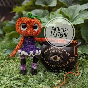 May include: Crochet pattern for a pumpkin amigurumi doll wearing a purple dress and black and white striped leggings. The doll is holding a black cauldron with a gold eye and the letters of the alphabet and numbers around it. The doll is sitting on green grass.