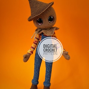 Può includere: Una bambola di spaventapasseri all'uncinetto con un cappello marrone, una salopette blu e una camicia a righe. La bambola ha grandi occhi scintillanti e un'espressione amichevole. L'immagine include il testo "DIGITAL CROCHET PATTERN".