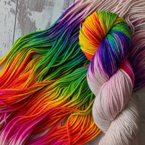 May include: Two skeins of yarn, one rainbow coloured and one white with a pink ombre effect. The rainbow yarn is wound into a ball shape.