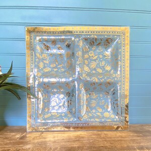 May include: A square glass serving dish with four compartments. The dish has a light blue base with a gold floral pattern.