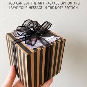 May include: A gift box with black and tan vertical stripes, tied with a sheer black ribbon. The box has a message on top that reads, "YOU CAN BUY THE GIFT PACKAGE OPTION AND LEAVE YOUR MESSAGE IN THE NOTE SECTION."