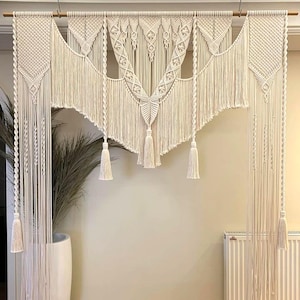 May include: A white macrame wall hanging with a geometric design and tassels. The hanging is made of cotton cord and is perfect for adding a bohemian touch to any room.