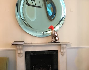 May include: A large circular convex mirror with a reflective surface that distorts the room's reflection, positioned above a fireplace mantel. A metallic dog figurine with a bright red head sits on the mantel in front of the mirror.