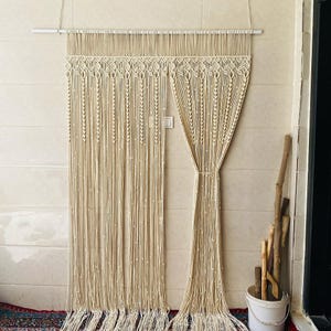Peut inclure: Un rideau en macramé blanc avec un motif décoratif. Le rideau est fait de cordon de coton et est suspendu à une tringle blanche.