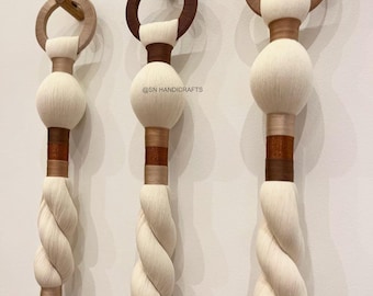 May include: Three decorative wall hangings with a natural, bohemian aesthetic. Each features a wooden ring and dowel, a white, spherical element, and a twisted, off-white rope design. The hangings have brown and tan accents and are mounted on a white wall.