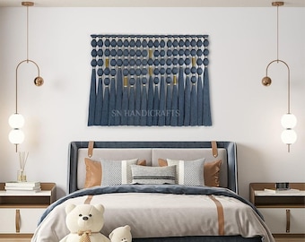 May include: A blue and gold wall hanging with tassels, featuring the text "SN HANDICRAFTS", above a bed with a white duvet and two teddy bears.