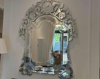 May include: Ornate silver-framed mirror with intricate floral and scrollwork details. The mirror has an arched top and a decorative crown element. The frame is embellished with reflective glass, adding a touch of elegance to the interior decor.